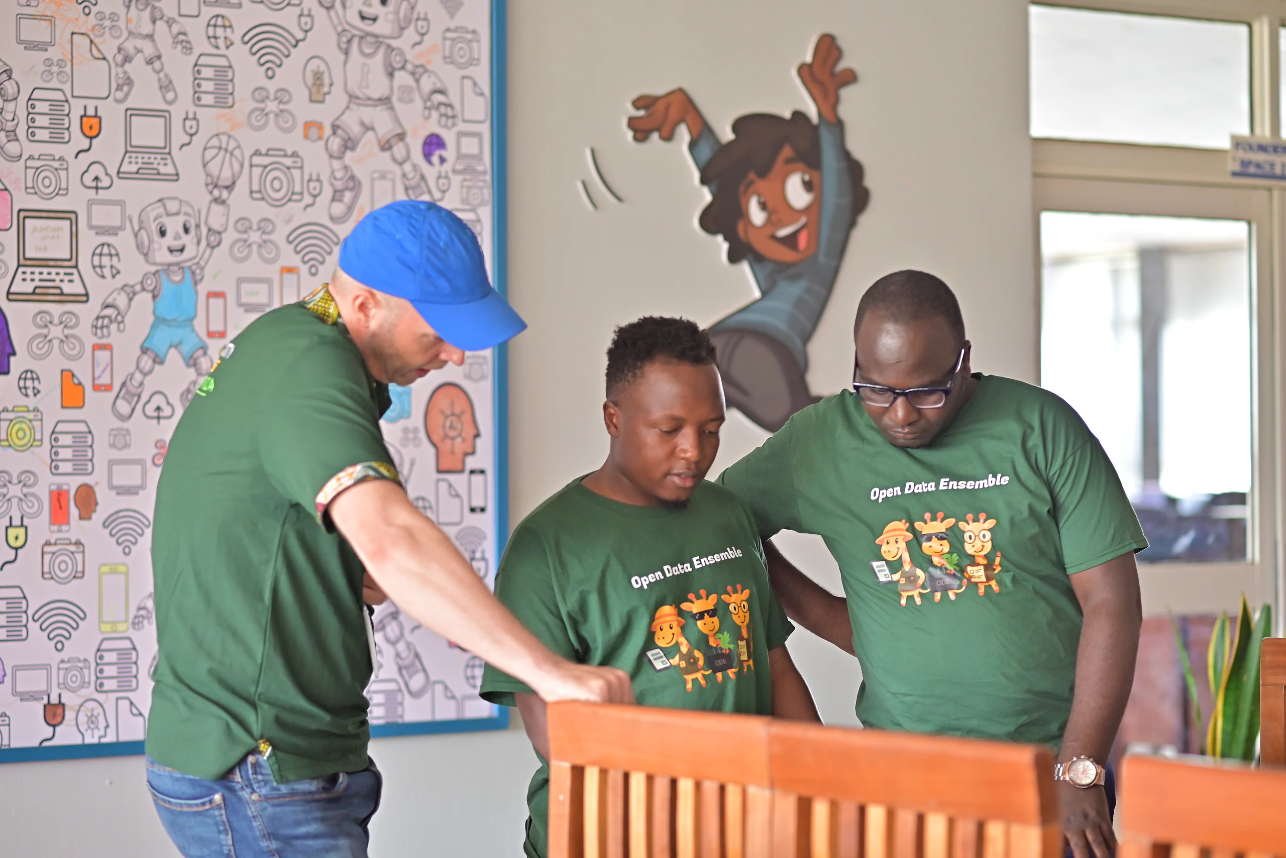 Three facilitators compare notes by a painted wall.