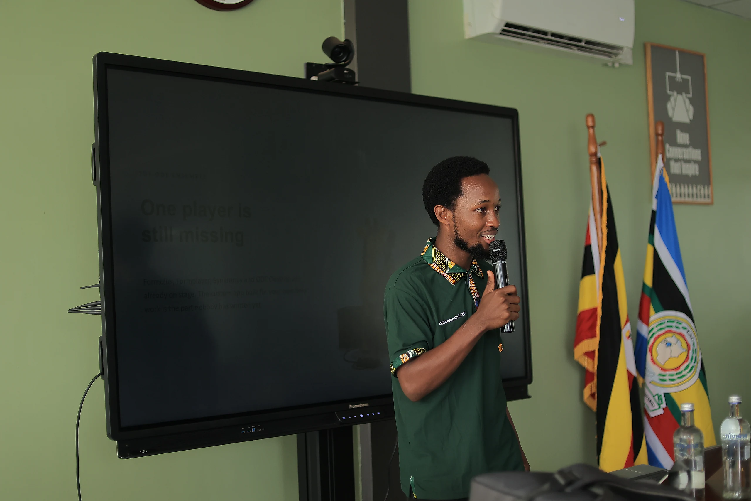 A speaker addresses the room beside a large screen.